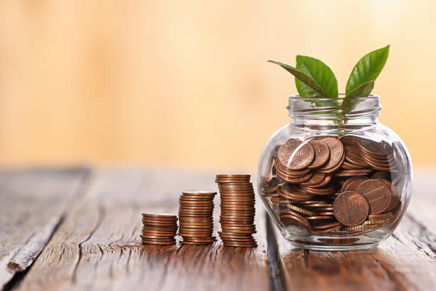 Investment concept. Glass jar with coins and sprout on wooden table against blurred orange background