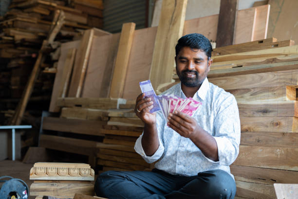 Focus on face, Happy young Indian woodworker or carpenter counting money at workplace or shop - concept of carpentry service, earning, professional occupation, financial and banking