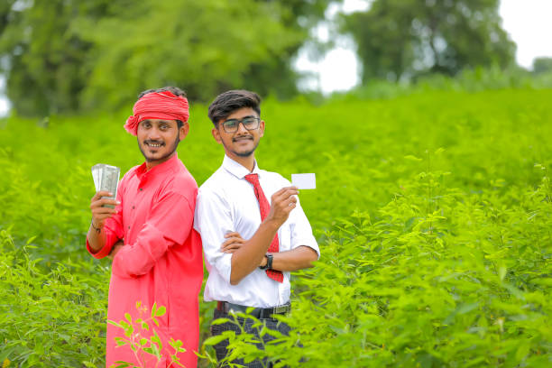 Young indian banker and farmer showing card and indian ruppees at green field
